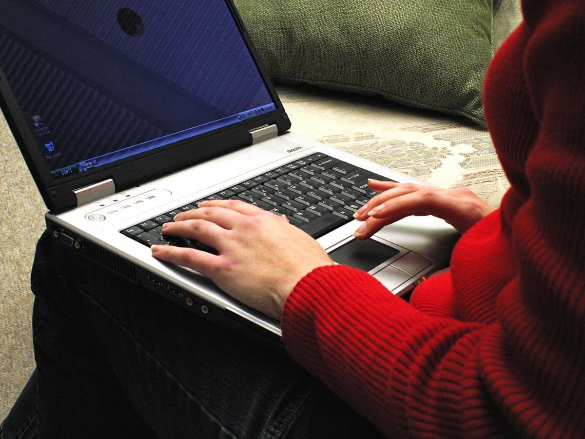 Kobieta w czerwonym swetrze korzystająca ze srebrnego laptopa na kanapie