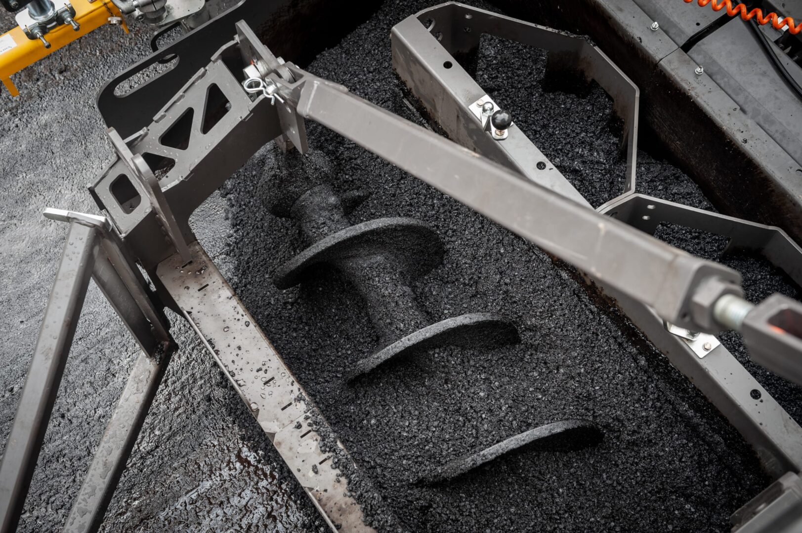 Zbliżenie frezarki asfaltowej, ukazujące ślimak i frezowany asfalt.