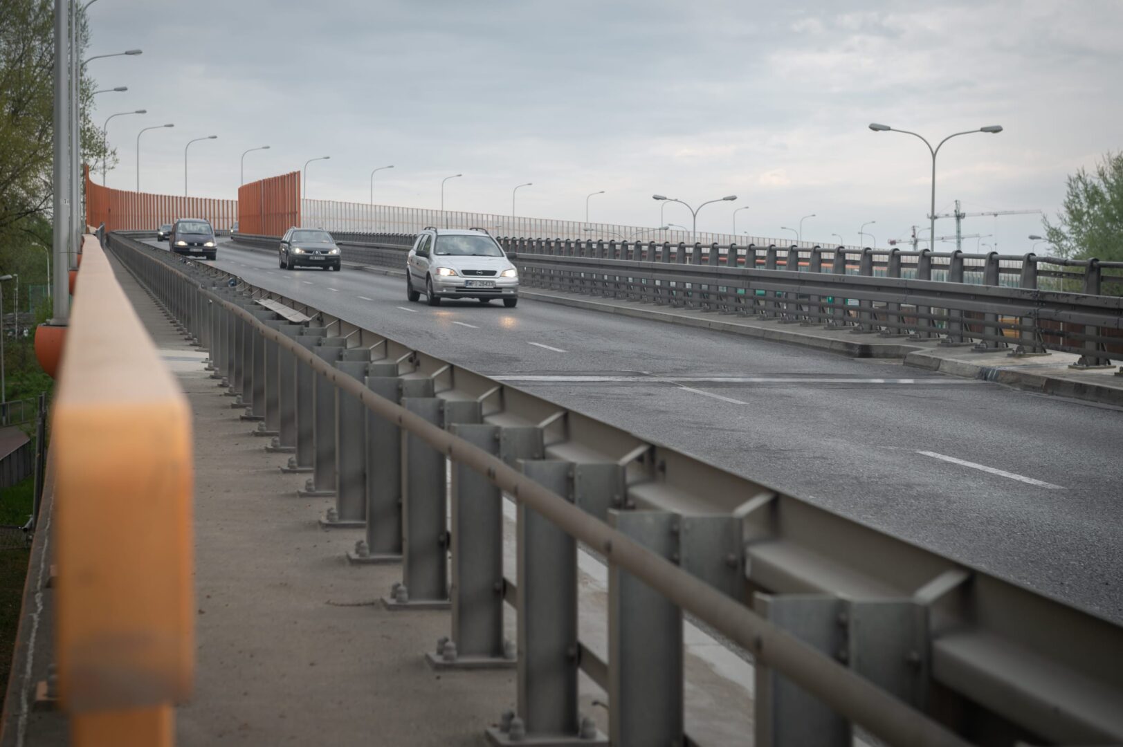 Samochody jadące po nowoczesnym moście z pomarańczowymi ekranami akustycznymi.