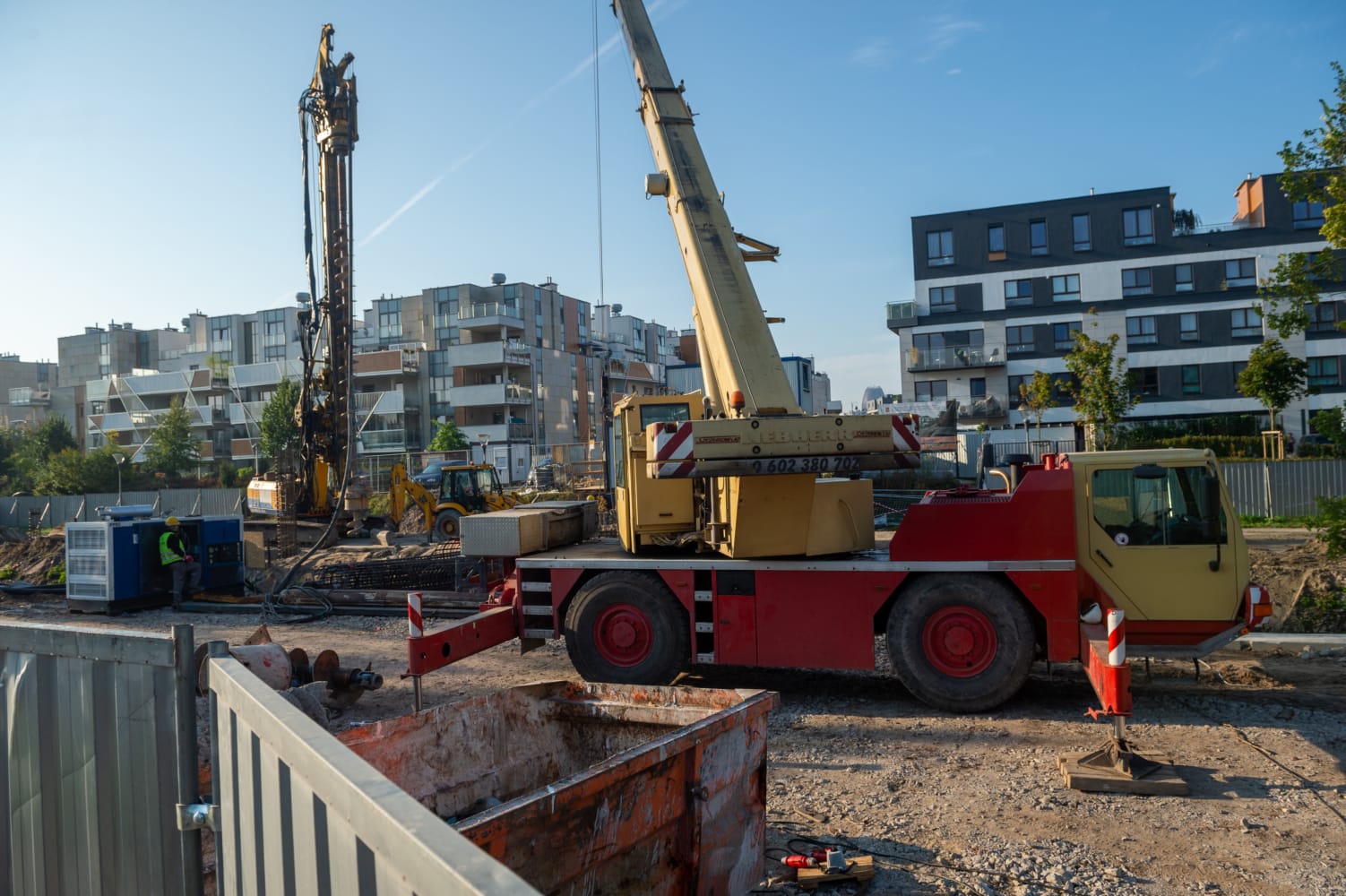 Plac budowy z dźwigiem, wiertnicą i pracownikami. Ciężki sprzęt na miejscu.
