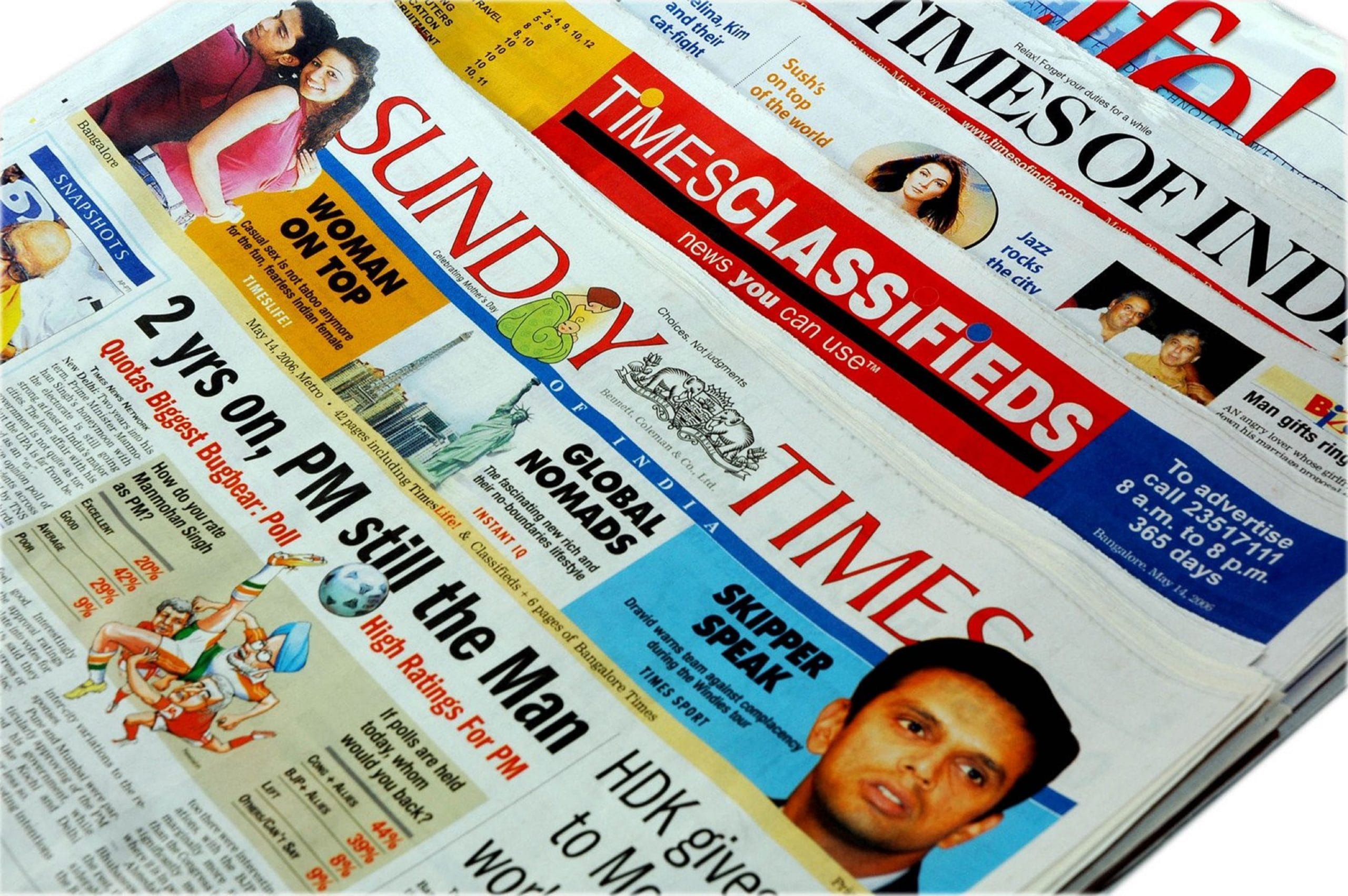Zbliżenie na ułożone w stosy indyjskie gazety, m.in. Times of India, z nagłówkami na temat polityki i sportu.