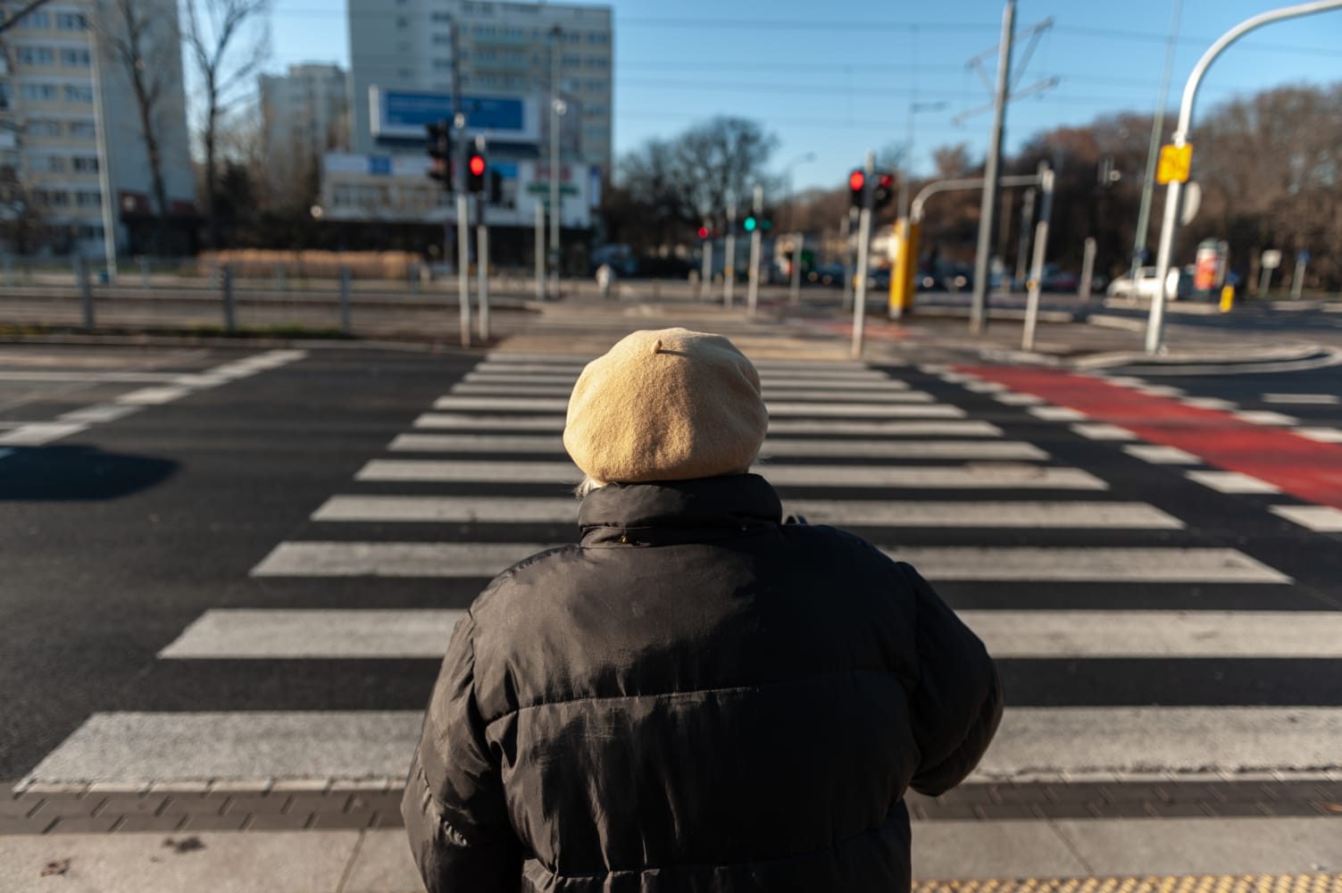 Starsza kobieta w berecie przechodzi przez ulicę miasta na przejściu dla pieszych.