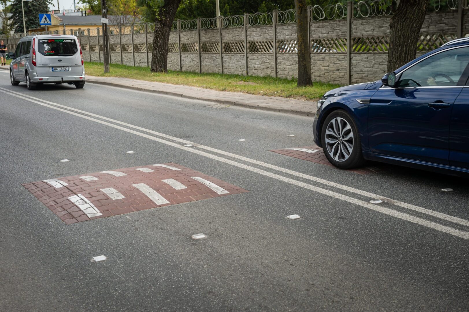 Samochód przejeżdżający przez próg zwalniający na ulicy miejskiej. Widoczne oznakowanie drogi.