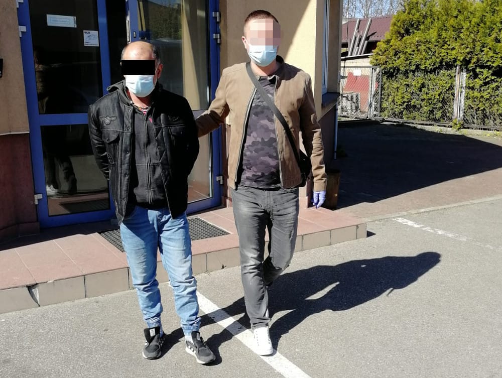 Dwóch mężczyzn w maskach na twarzach, aresztowanych i eskortowanych przez policję.