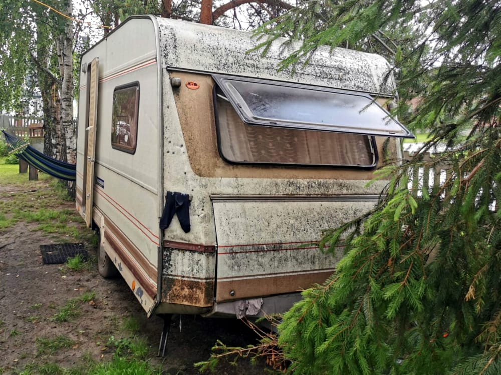Stara, zniszczona przyczepa kempingowa zaparkowana pod drzewami na polu kempingowym.