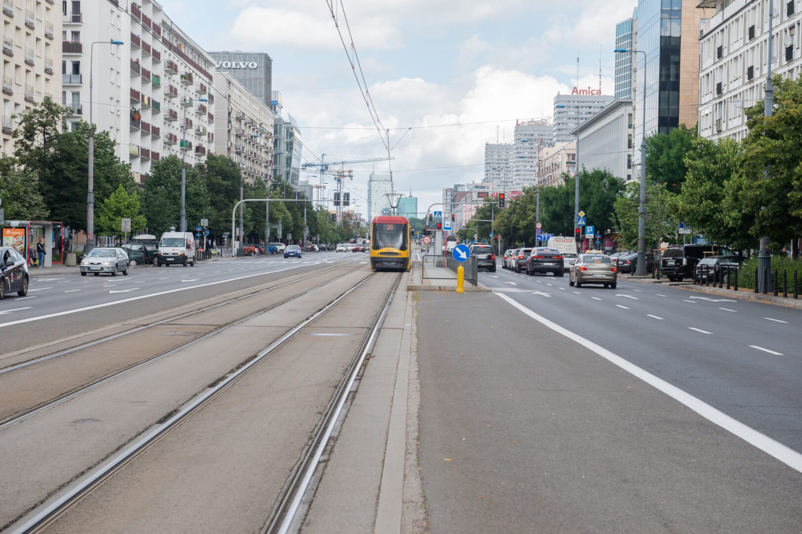 Widok na warszawską ulicę z tramwajem i ruchem ulicznym, prezentująca nowoczesną architekturę.
