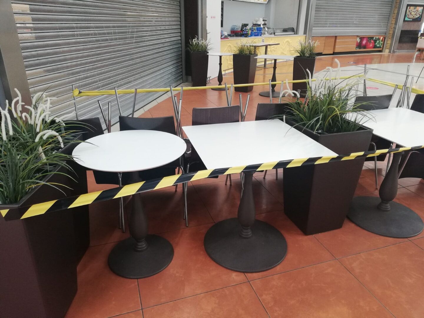 Puste stoliki i krzesła w punkcie gastronomicznym galerii handlowej odgrodzone taśmą ostrzegawczą.