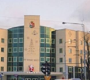 Budynek wielopiętrowy z dużymi oknami i herbem nad wejściem.