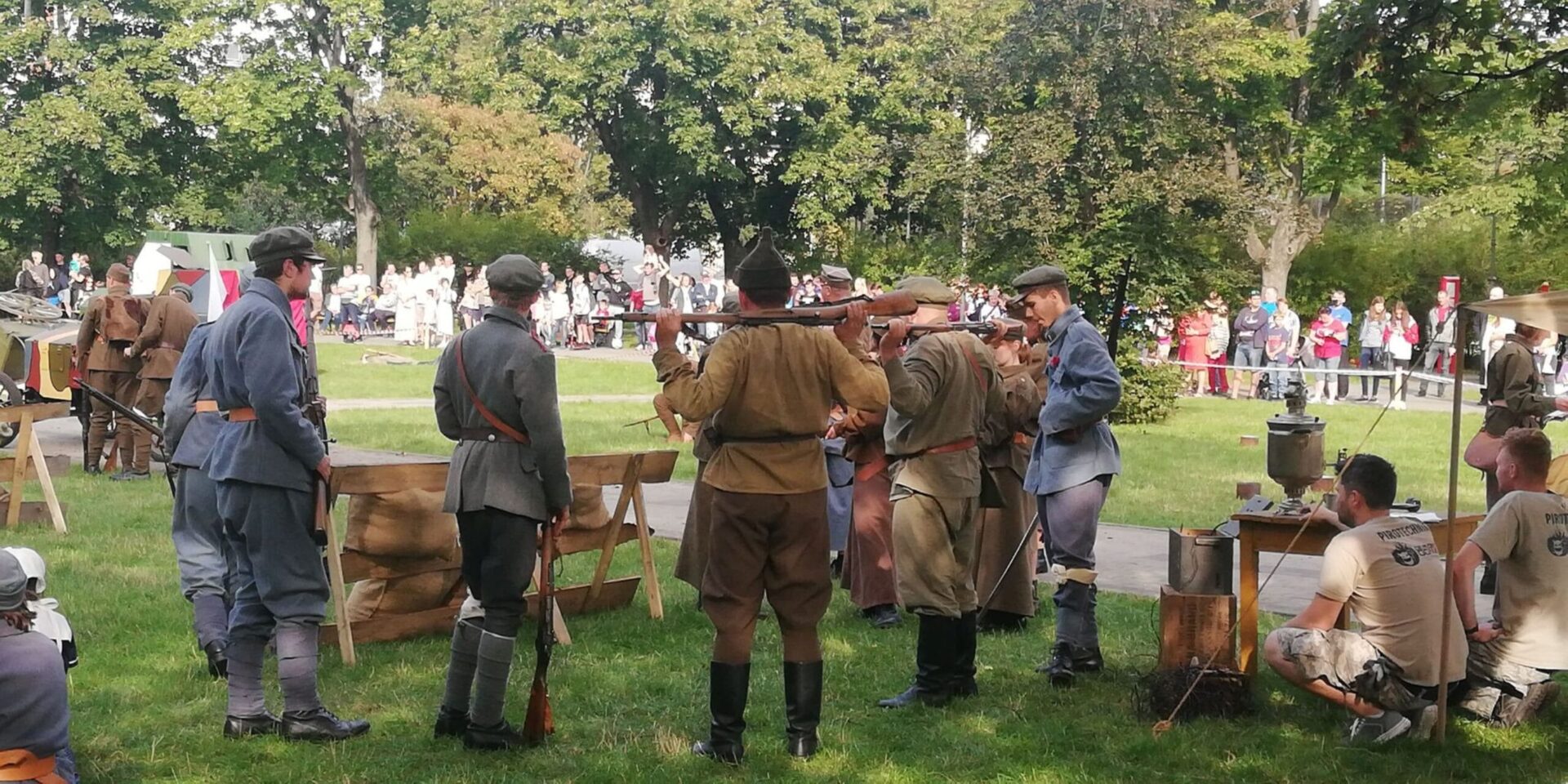 Rekonstruktorzy II wojny światowej w mundurach z epoki, z karabinami, na tle polskiego parku.