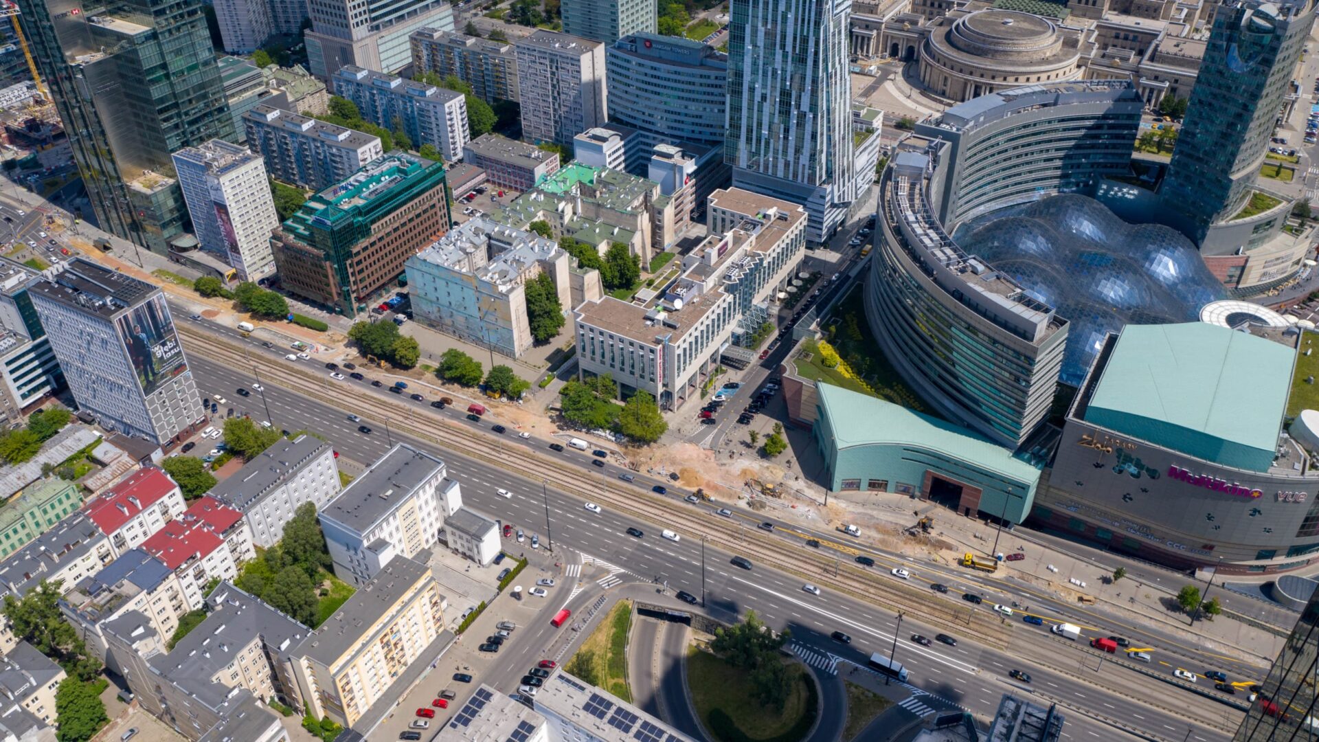 Widok z lotu ptaka na panoramę Warszawy, ukazujący wieżowce, drogi i centrum handlowe Złote Tarasy.