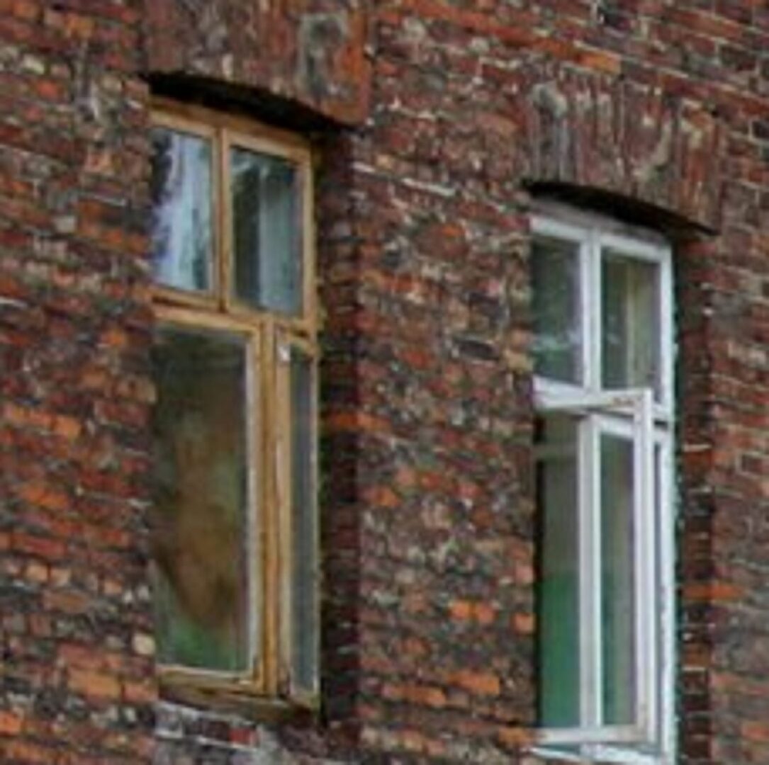 Stary ceglany budynek z dwoma oknami, jedno w drewnianej ramie, drugie w białej ramie.