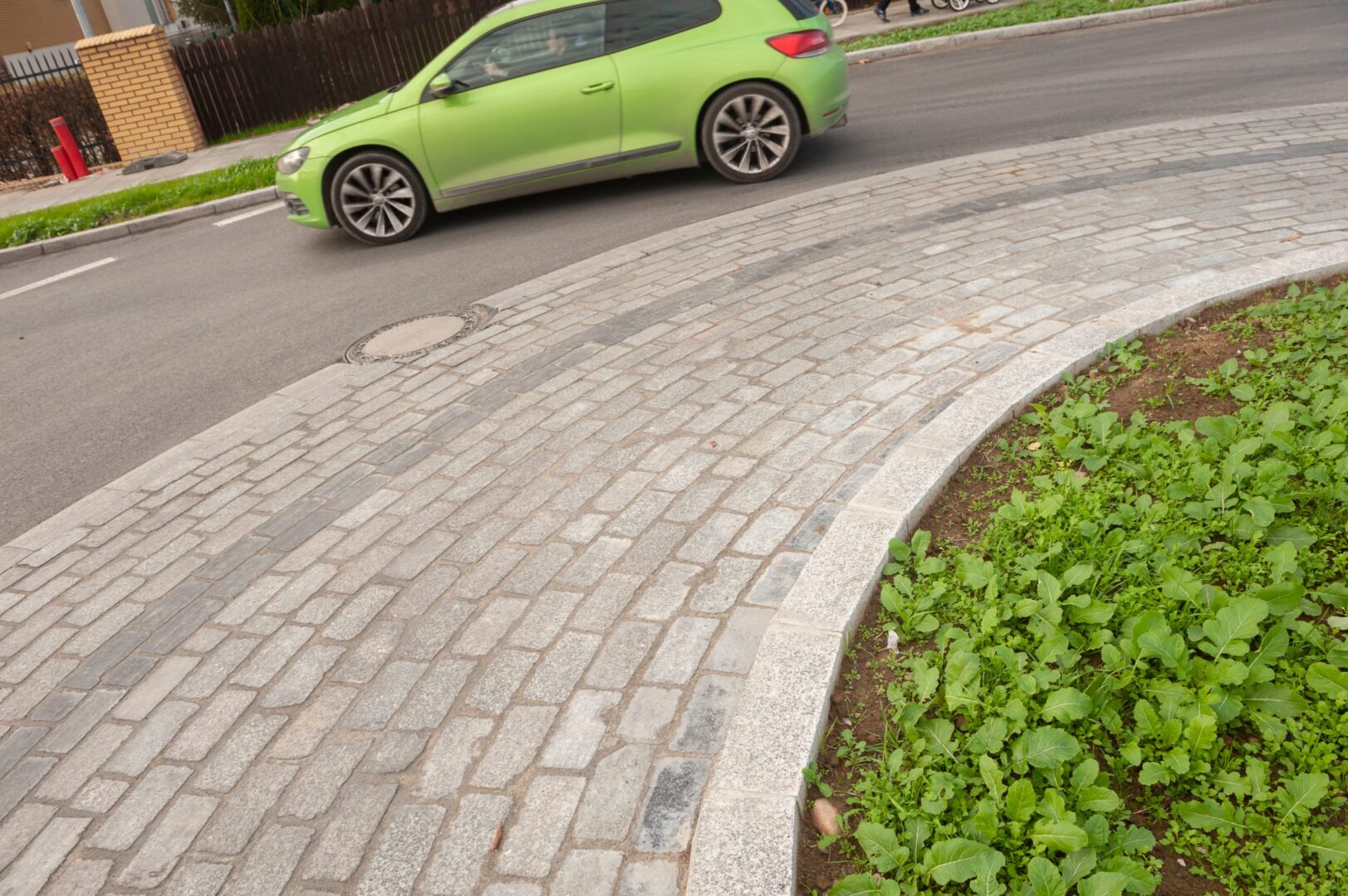 Zielony samochód jadący wzdłuż zakrzywionej brukowanej ścieżki.