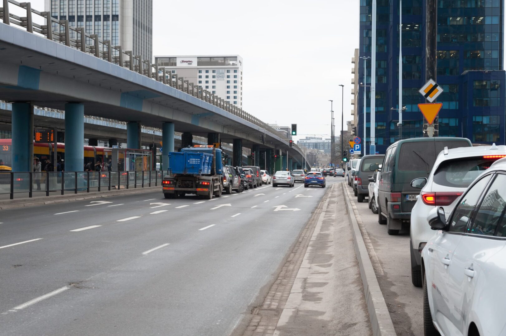 Scena uliczna Warszawy z samochodami i przystankiem autobusowym pod wiaduktem autostradowym w pobliżu Ronda Czterdziestolatka.