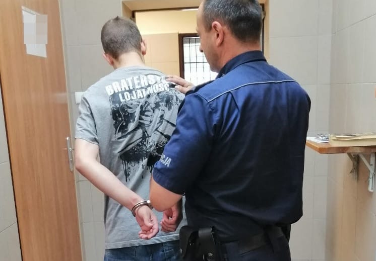 Policjant aresztujący mężczyznę w kajdankach. Na koszuli mężczyzny widnieje napis „BRATERSKA LOJALNOSC”.