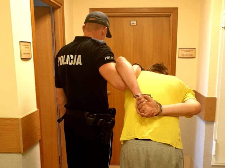 Policjant aresztujący podejrzanego w kajdankach na korytarzu.