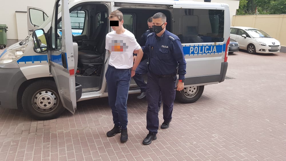 Policjant aresztujący młodego mężczyznę. Na radiowozie widać napis „POLICJA”.