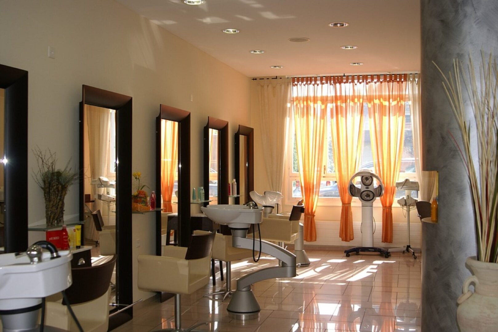 Nowoczesne wnętrze salonu fryzjerskiego ze stanowiskami do stylizacji, lustrami i pomarańczowymi zasłonami.