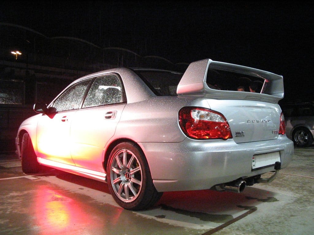 Srebrne Subaru WRX STI z dużym tylnym spojlerem zaparkowane nocą.