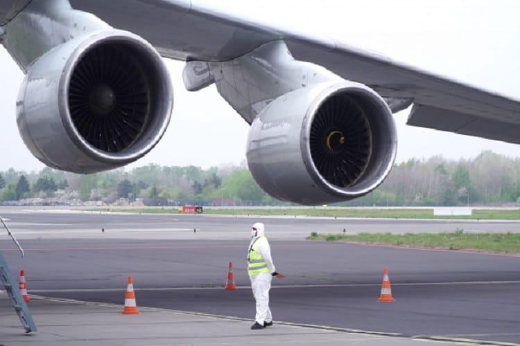 Silniki samolotu i obsługa naziemna w skafandrach ochronnych na płycie lotniska
