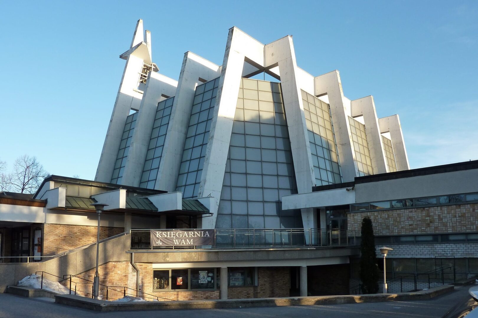 Nowoczesna architektura kościelna, charakteryzująca się kanciastym projektem i szklaną fasadą. Widoczna księgarnia "Księgarnia Wam".