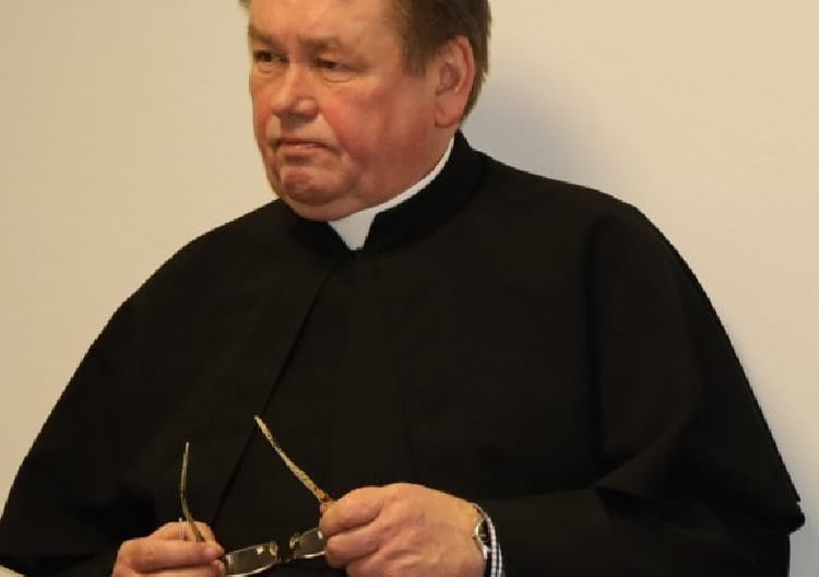 Portret księdza w stroju duchownym, trzymającego okulary.