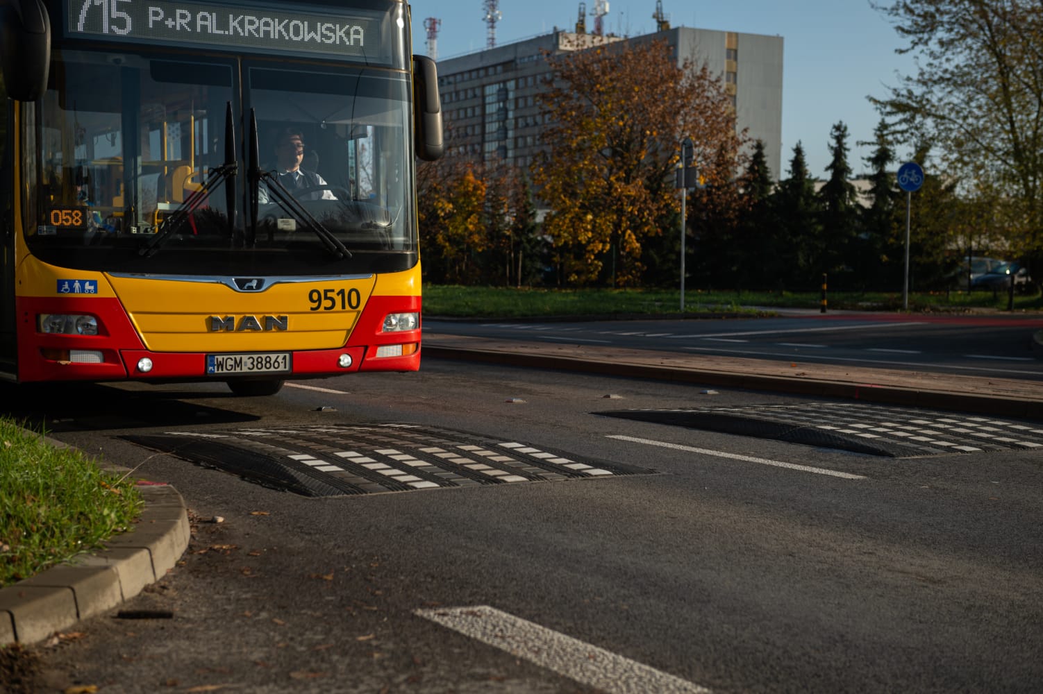 Żółty i czerwony autobus miejski MAN, numer 9510, zbliża się do progu zwalniającego na ulicy miejskiej.