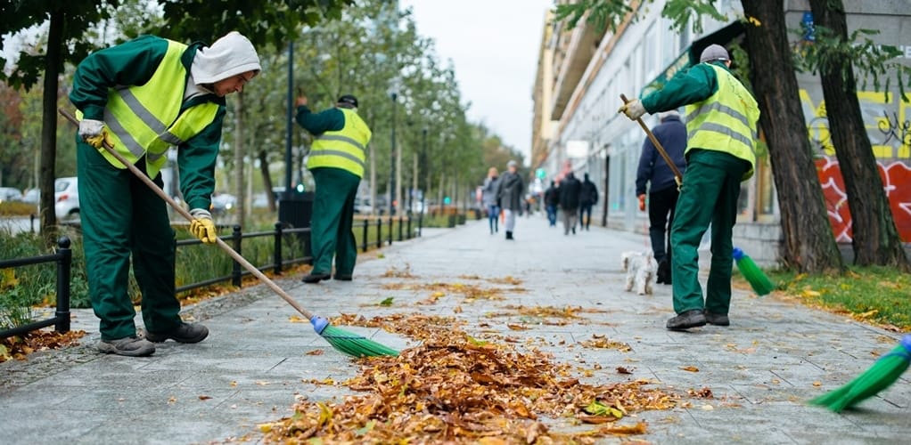 Pracownicy sprzątający ulice zamiatają opadłe jesienne liście z chodników w mieście.
