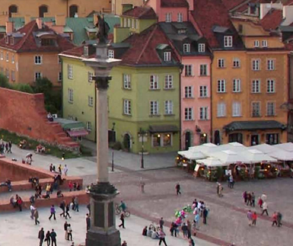 Rynek Starego Miasta w Warszawie, z kolorowymi budynkami, kolumną i miejscami do siedzenia na zewnątrz.