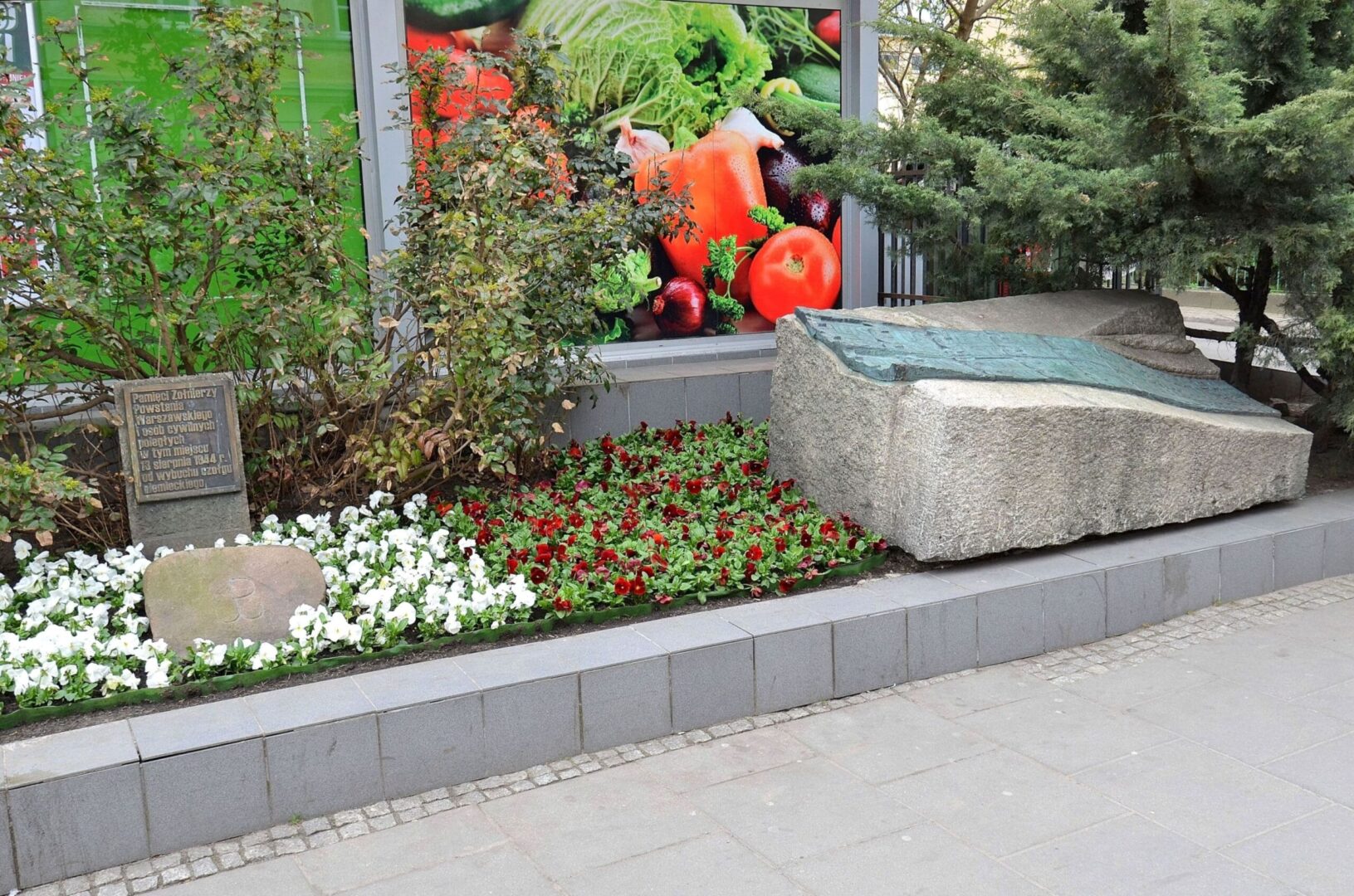 Pomnik Powstania Warszawskiego z kwiatami i tablicą upamiętniającą żołnierzy i cywilów.