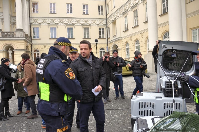 Policjanci i pracownicy służb zajmujących się ochroną zwierząt zbierają się w pobliżu zwierząt w klatkach na zewnątrz budynku.