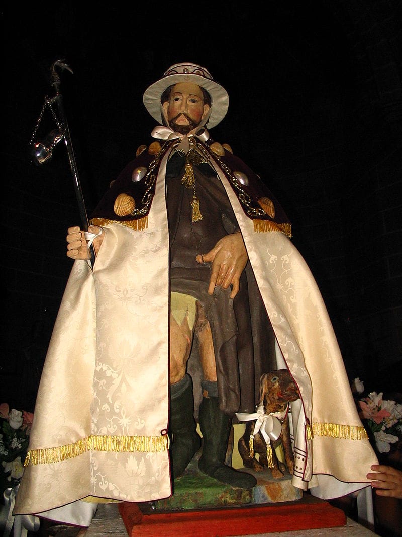 Posąg św. Rocha trzymającego laskę, odzianego w długi płaszcz i kapelusz.