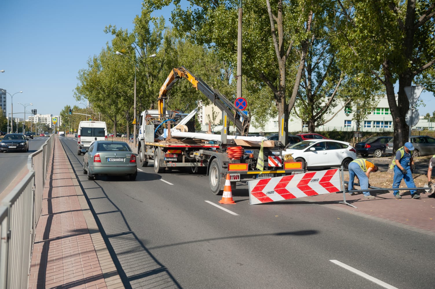 Ekipa budowlana pracująca na ulicy miejskiej, używająca dźwigu samochodowego i sprzętu.