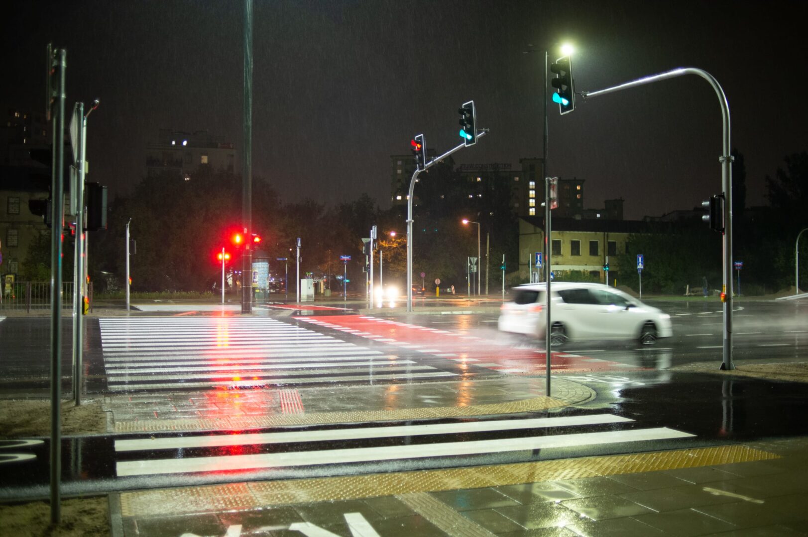 Deszczowa noc na przejściu dla pieszych z sygnalizacją świetlną i przejeżdżającym samochodem.
