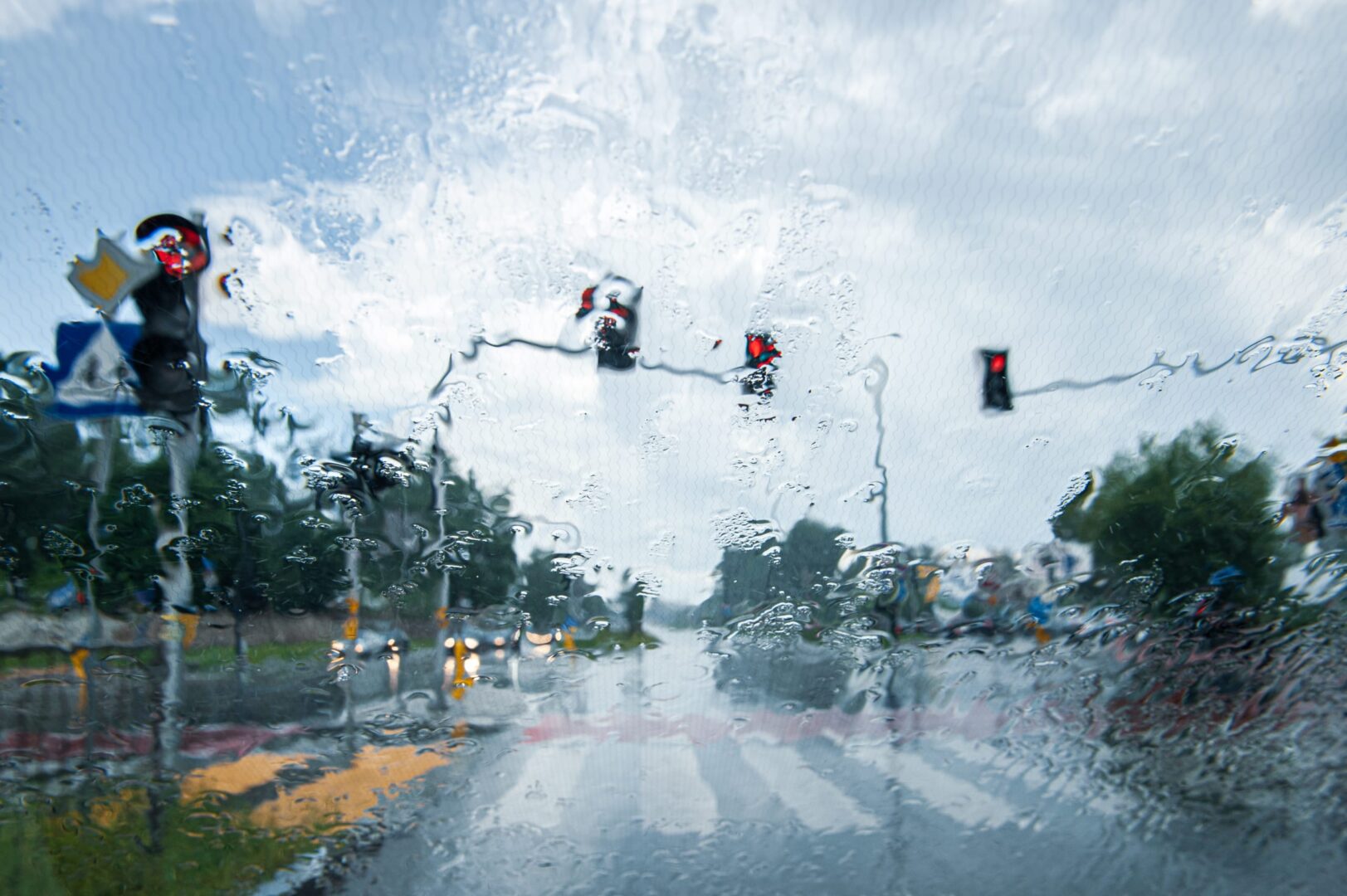 Widok zza szyby skrzyżowania z zaciekami po deszczu i czerwonymi światłami.