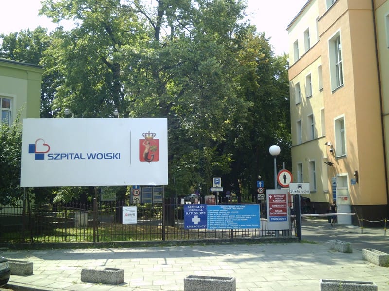 Wejście do szpitala Szpital Wolski z oznakowaniem i drzewami