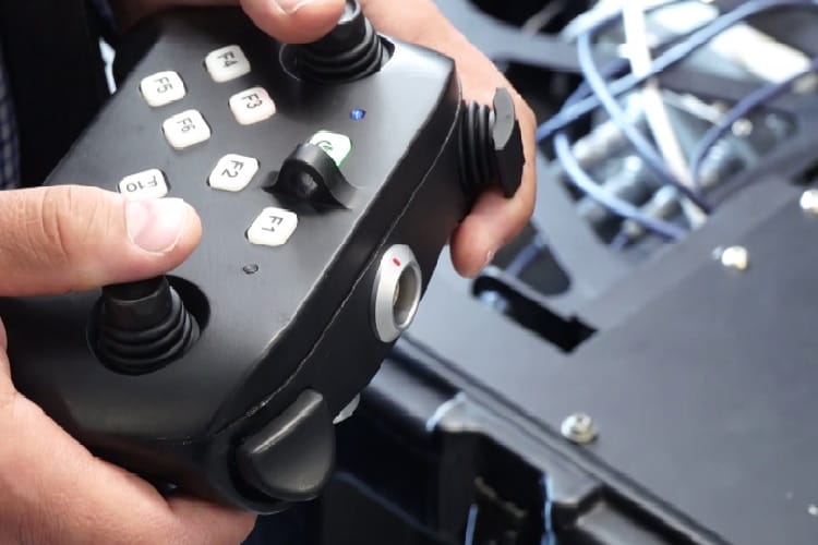 Zbliżenie dłoni obsługujących czarny joystick z przyciskami wielofunkcyjnymi (F1-F6).