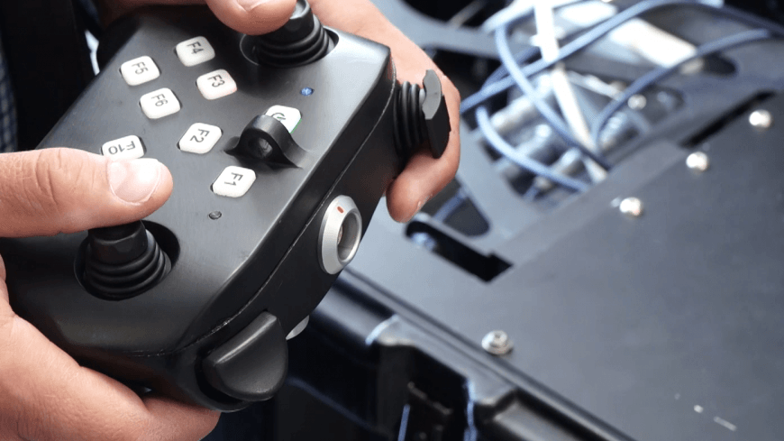 Zbliżenie dłoni obsługujących panel sterowania robota za pomocą joysticka i przycisków funkcyjnych (F1-F10).