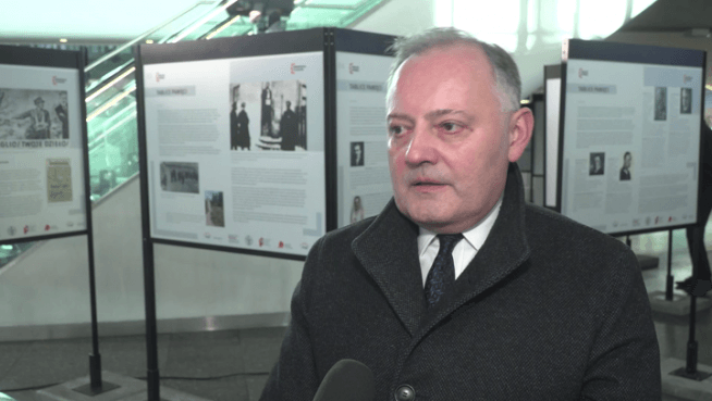 Mężczyzna w garniturze przemawia na wystawie Tablice Pamięci na Dworcu Centralnym w Warszawie.