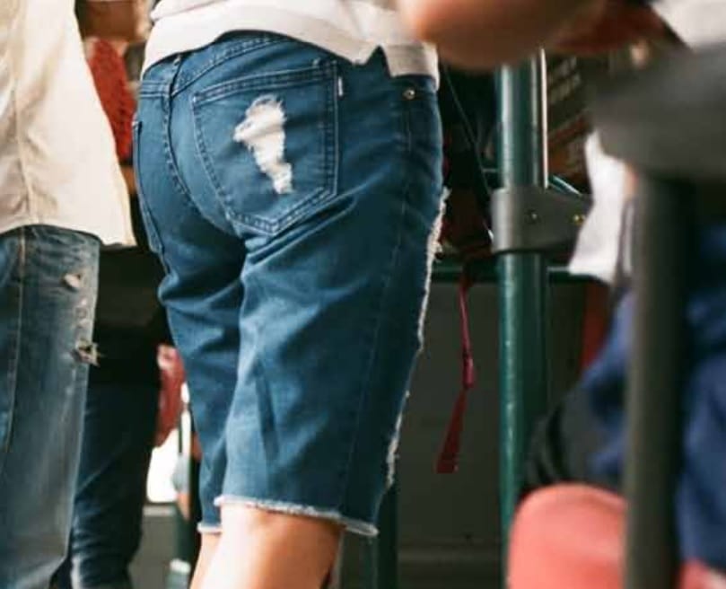 Zbliżenie na szorty dżinsowe osoby w zatłoczonym autobusie w czasie pandemii.