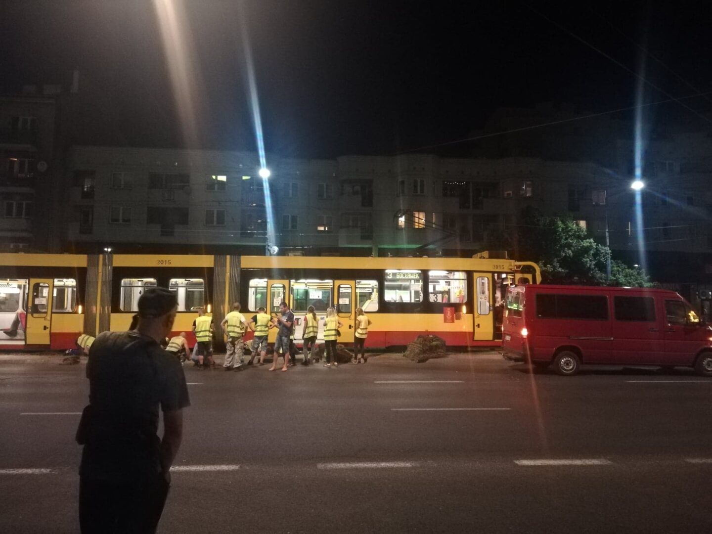 Nocna scena wypadku tramwajowego z udziałem ratowników i czerwonego vana.