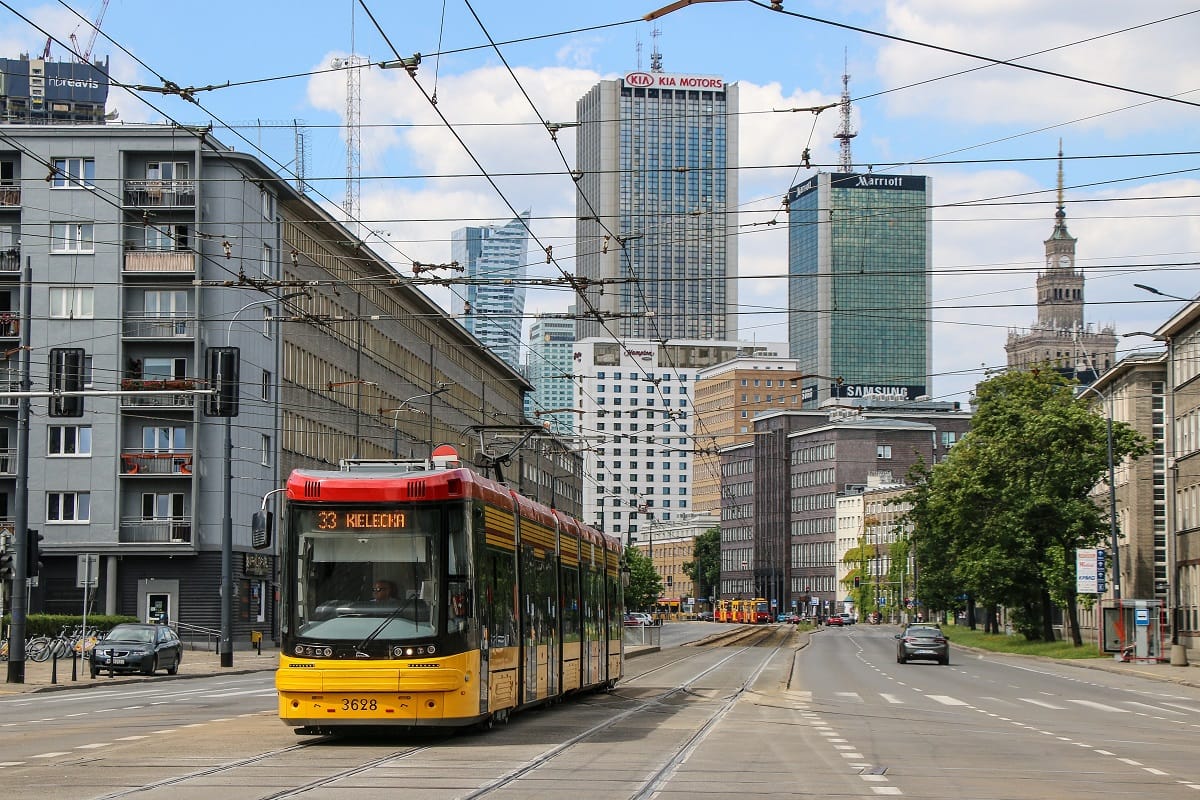 Widok na panoramę Warszawy, Polska z żółtym tramwajem na ulicy i nowoczesnymi wieżowcami w tle.