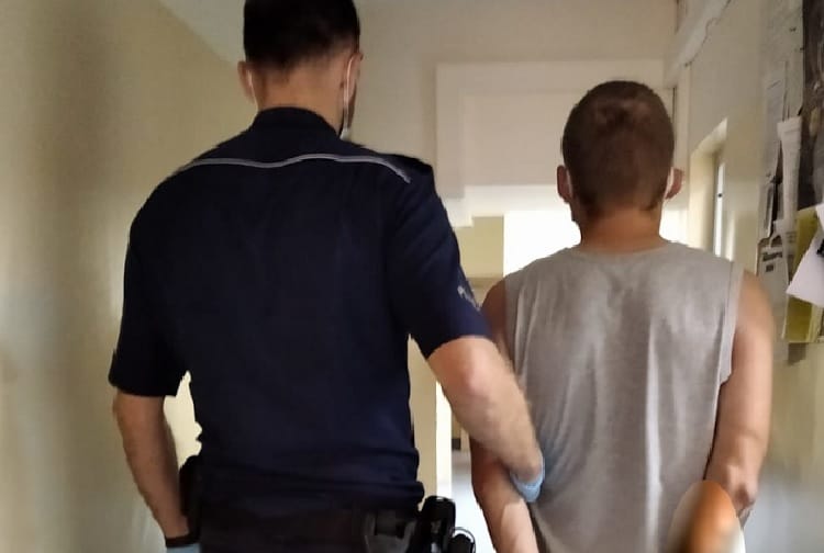 Policjant eskortujący podejrzanego w kajdankach korytarzem.