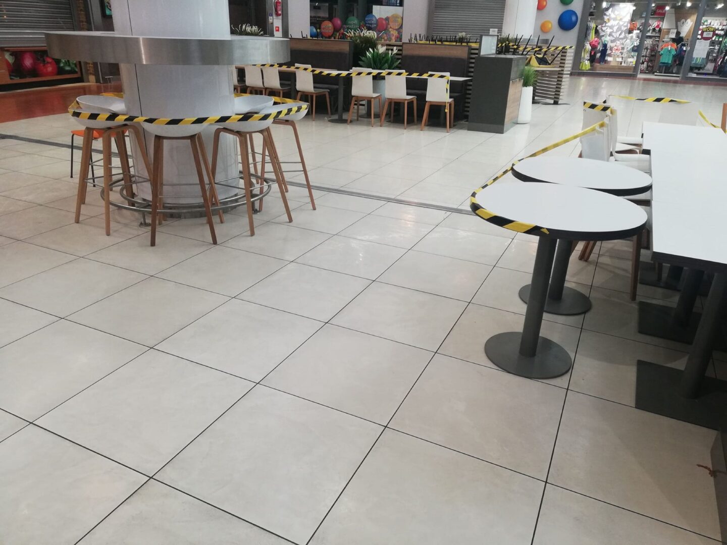 Puste stoliki i krzesła w punkcie gastronomicznym galerii handlowej odgrodzone taśmą ostrzegawczą.