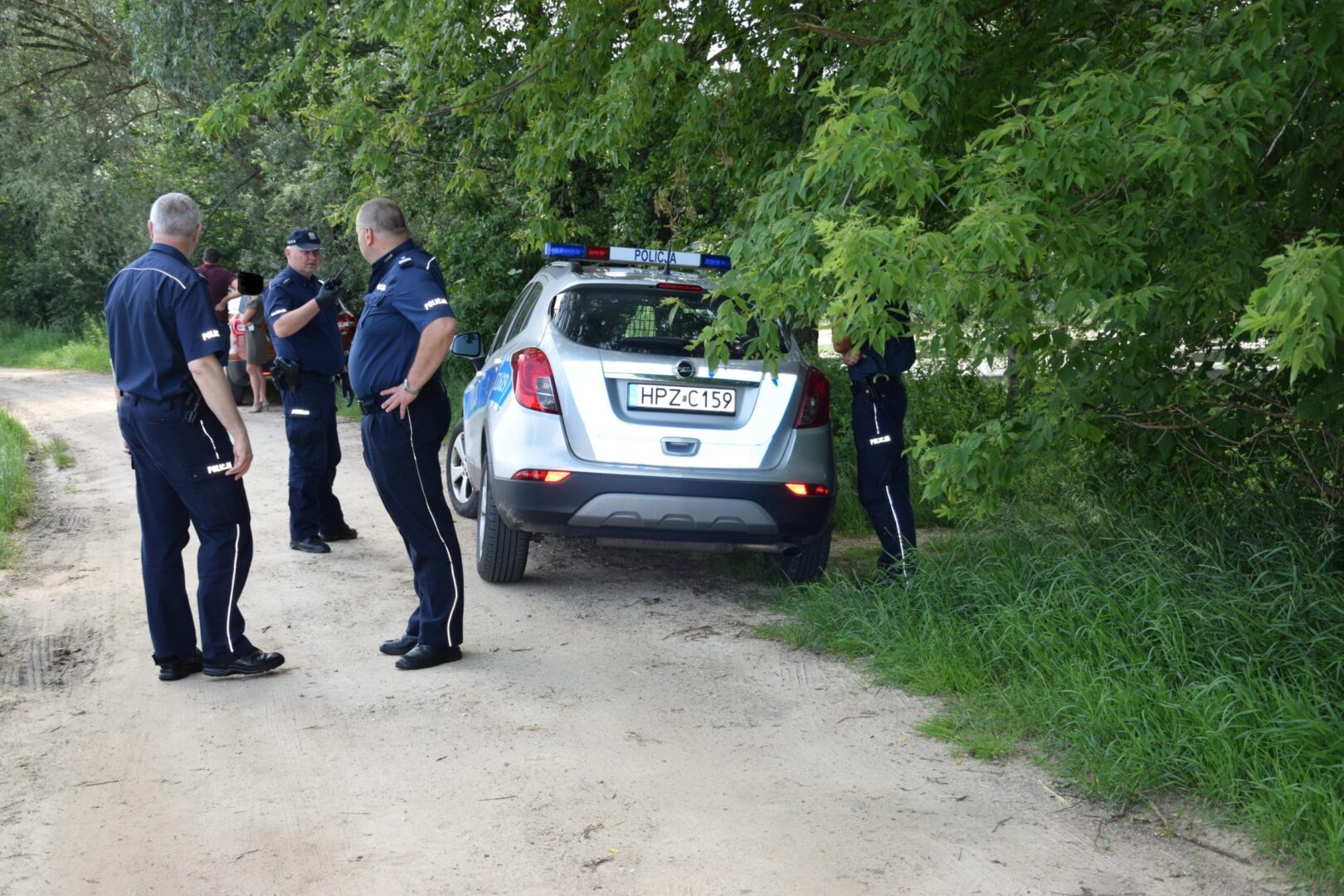 Policjanci z polskiej policji podczas dochodzenia przy drodze w pobliżu srebrnego Opla Mokki. Widoczna tablica rejestracyjna HPZ C159.