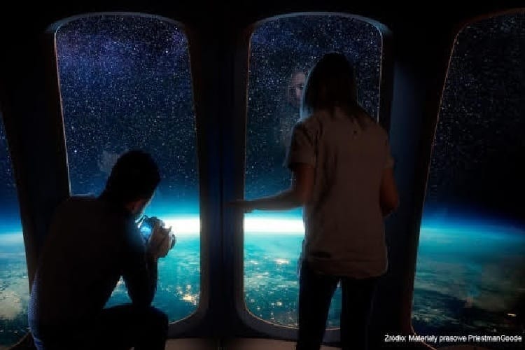 Dwie osoby obserwują Ziemię z okna statku kosmicznego, jedna z nich robi zdjęcie.