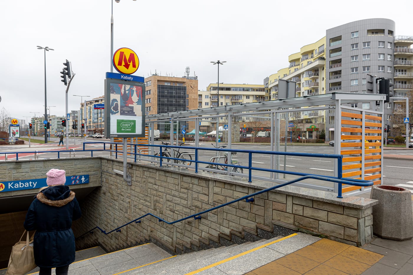 Wejście na stację metra Kabaty. W tle stojaki na rowery i nowoczesny budynek.