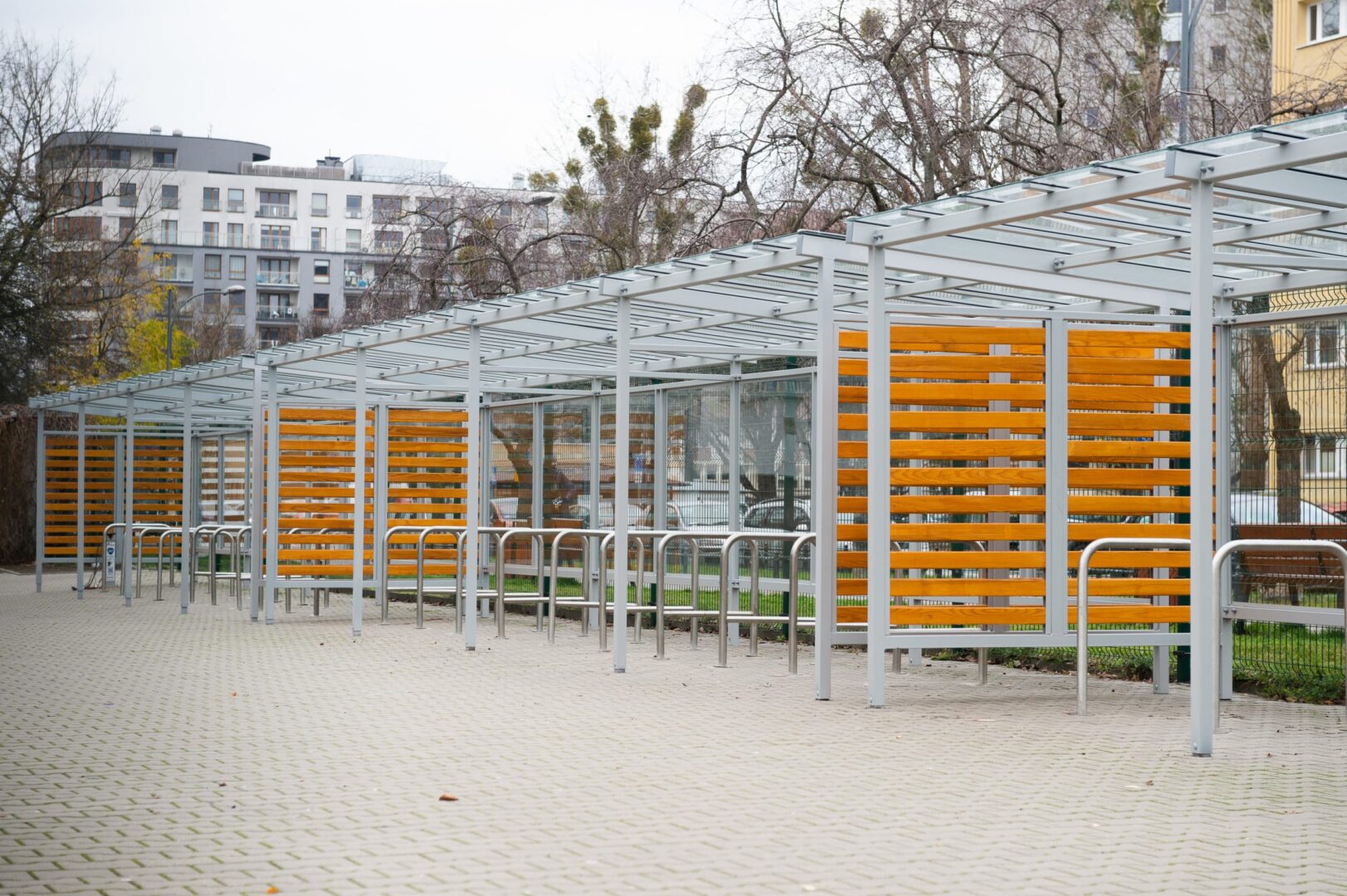 Nowoczesna wiata rowerowa ze szklanym dachem i drewnianymi panelami.