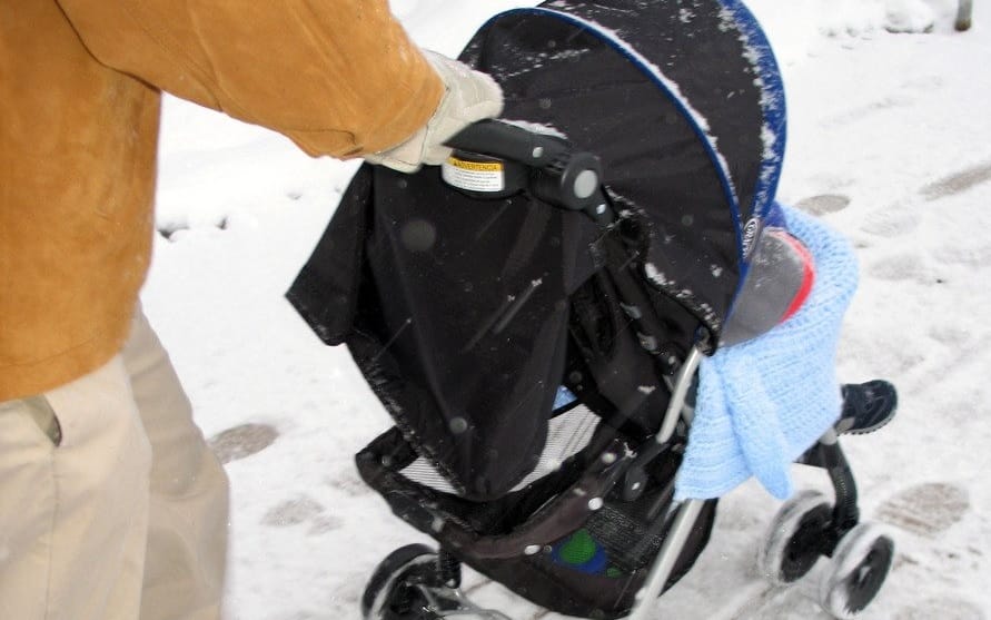 Osoba pchająca wózek dziecięcy po śniegu