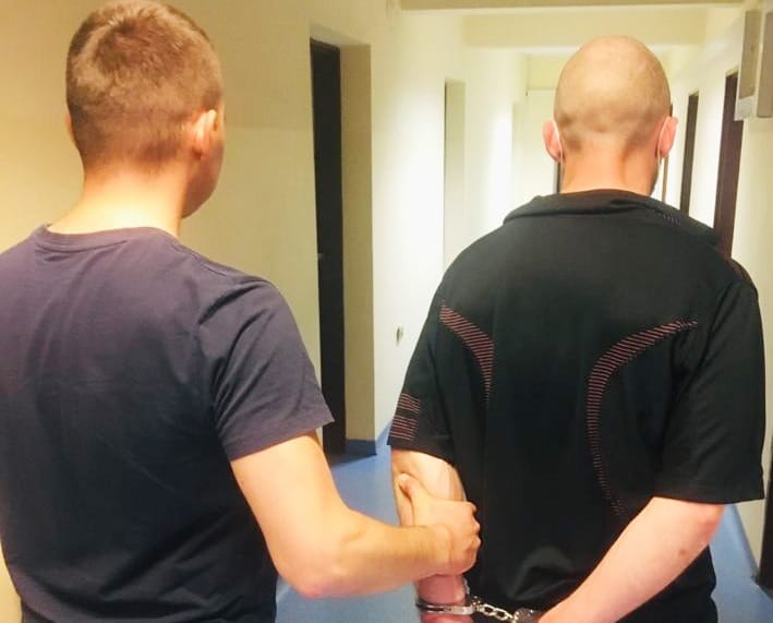 Policjant aresztujący podejrzanego, widoczne kajdanki.