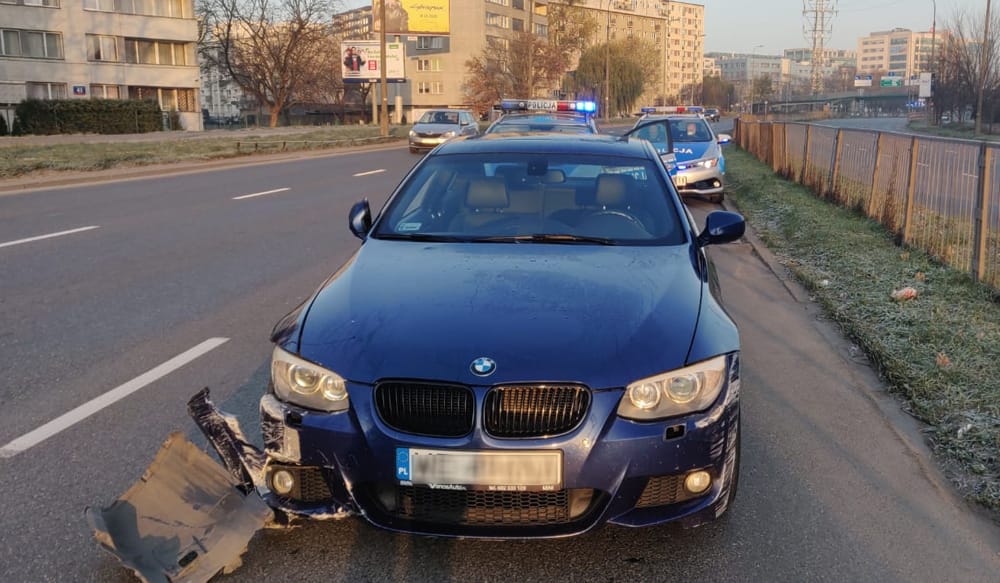 Zniszczone niebieskie BMW zatrzymane przez policję. Brak przedniego zderzaka.